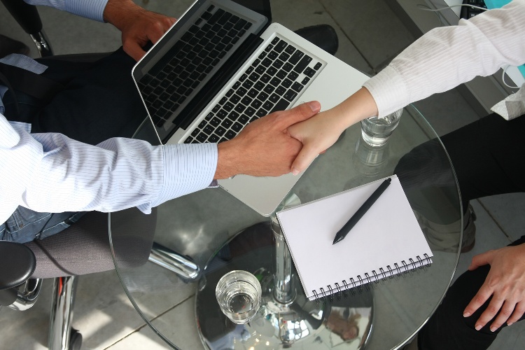 Handshake over a table with a macbook and a notepad